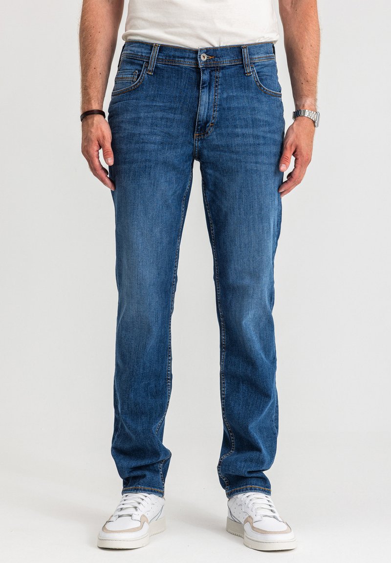 Niebieskie jeansy z denimu o klasycznym, prostym kroju, wyposażone w pięć kieszeni, subtelne przeszycia i czyste wykończenie. Noszone z białymi trampkami.