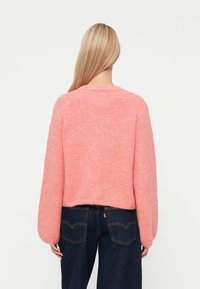 Różowy sweter z dzianiny o długich, objętościowych rękawach i skróconym fasonie, w połączeniu z ciemnymi dżinsami z widocznymi szwami i kieszeniami.