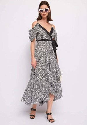 Donna che indossa un vestito a spalle scoperte con motivo bianco e nero, cintura nera, occhiali da sole bianchi a forma di gatto e sandali neri con tacco.