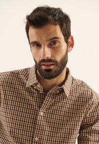 Chemise à carreaux marron, crème et bleu. Col boutonné, boutons sur le devant et logo brodé sur la poitrine. Tissu en coton doux.