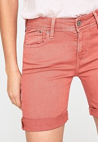 Shorts de mezclilla rosa con puños enrollados, con un bolsillo frontal, trabillas para el cinturón y un detalle de botón plateado en la cinturilla.