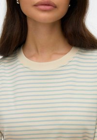 Ljusblå och krämfärgad randig skjorta med ribbad halsringning. Tyget verkar mjukt med en slät textur och har subtila söm detaljer.