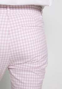 Pantalons à carreaux lavande clair avec une texture lisse, dotés d'une poche arrière et d'une coupe ajustée avec des détails de couture subtils.