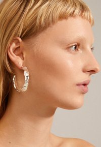 Silberne Hängohrringe mit einer unregelmäßigen, strukturierten Oberfläche. Leichtes Design mit einer gedrehten Form, die Licht und Schatten reflektiert.