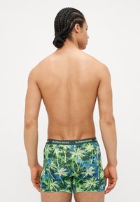 Tropical pálmalevél mintázattal rendelkező boxer nadrág zöld és kék színben, sötétzöld rugalmas derékgummival, amelyen a márka neve szerepel.