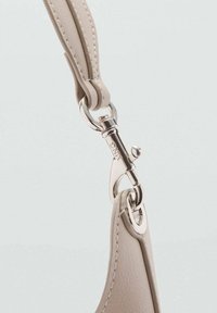 Cinturino in pelle beige chiaro con chiusura in metallo argentato, dotato di un piccolo gancio rotondo e dettagli di cucitura visibili.