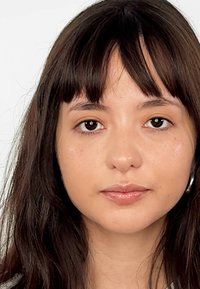 Retrato de una persona joven con cabello largo y castaño oscuro con flequillo. Tienen un tono de piel medio y maquillaje sutil, destacando labios brillantes.