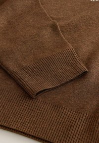 Braunes, gestricktes Pulloverstoff im Nahaufnahme, mit einem gerippten Saum und Bündchen, einer weichen Textur und dezenten Farbnuancen.