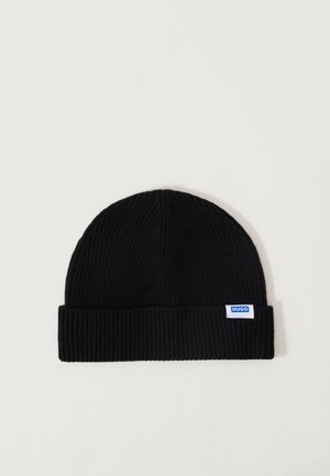 Zwarte gebreide beanie met een dikke geribbelde textuur en een opgevouwen rand. Bevat een klein blauw en wit logo-label aan de zijkant.