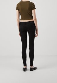 Jeans ajustados negros con una cintura alta, combinados con una camiseta corta de color verde oliva. El calzado consiste en zapatos planos negros con tachuelas y calcetines estampados.