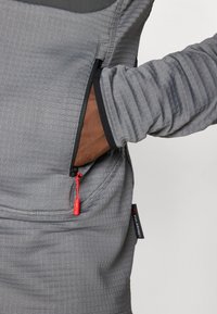Grå, tekstureret pullover med en lynlås lomme med en rød trækflig, kontrastløs sort trim og designet med tætsiddende manchetter.