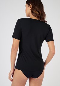 T-shirt nera a maniche corte, realizzata in tessuto liscio, presenta un colletto rotondo e un orlo leggermente curvo sul retro. Design semplice e aderente.