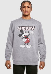Grå hettegenser med et vintage Mickey Mouse-trykk i svart, rødt og hvitt. Lange ermer, ribbede mansjetter og rund hals.