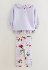 Sweatshirt lilas avec col volanté et détails de boutons, superposé sur un legging léger à motifs floraux avec des fleurs roses et des feuilles vertes.