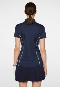 Marinblå polo skjorta med vit kontrastsöm, korta ärmar och krage, paired med marinblå veckad kjol. Lättvikts, sportig passform.