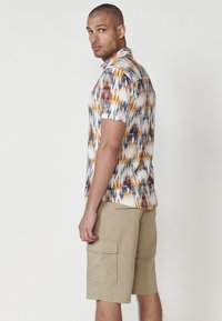 Chemise à manches courtes avec un motif abstrait multicolore en orange, marine et blanc. Assortie à un short cargo beige avec des poches latérales.