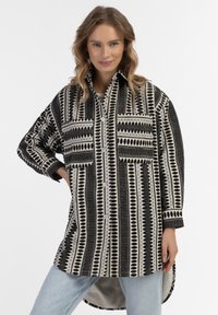 Juodai baltas raštuotas didelio dydžio marškinis su priekyje mygtuku užsegimu, dviem krūtinės kišenėmis ir ilgesniu nugaros kraštu. Švelni audinio tekstūra.