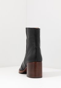 Bota negra de cuero hasta el tobillo con punta redondeada y un tacón medio de bloque de madera. Presenta una textura suave y un diseño minimalista.