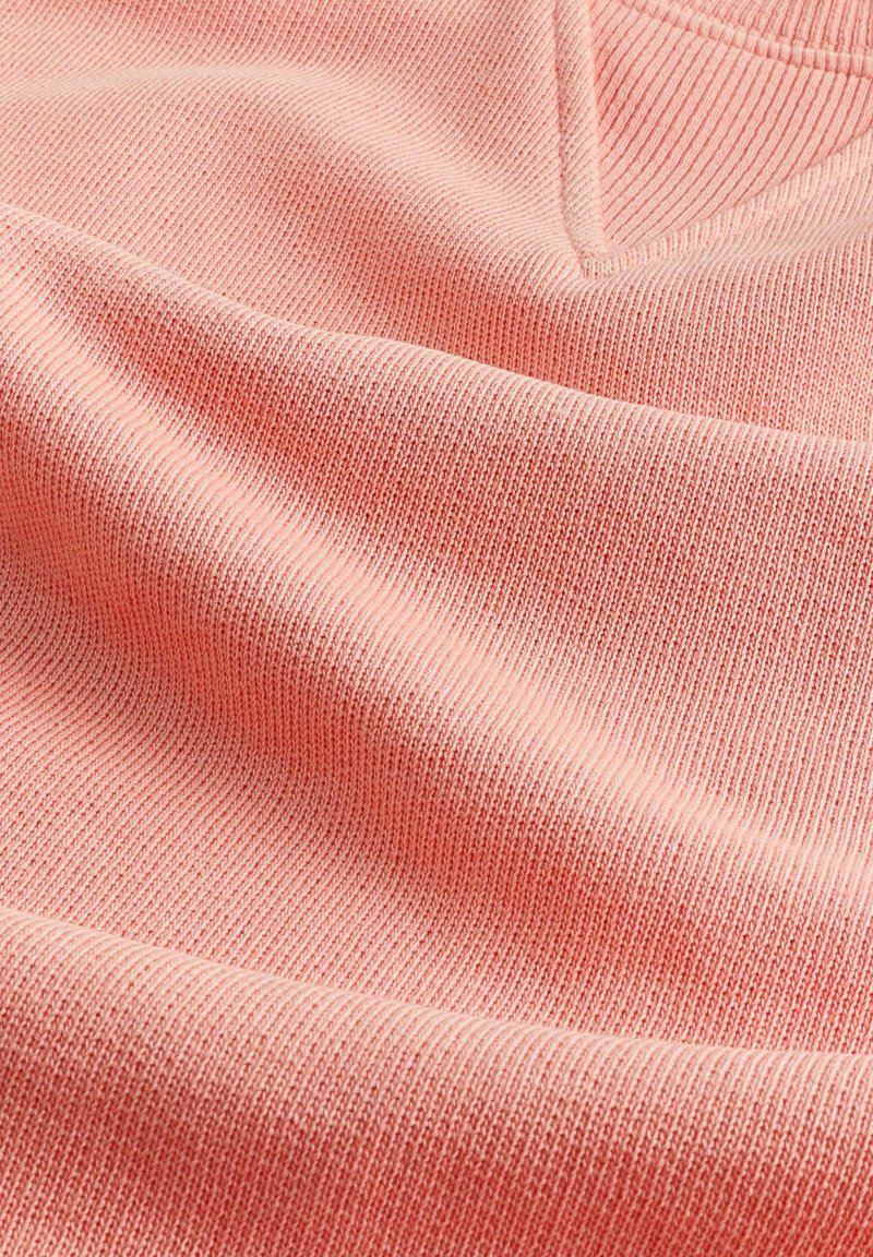 Tissu corail clair avec une texture côtelée, présentant de subtiles lignes horizontales et un aspect doux et extensible.