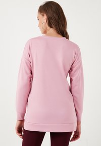 Top rosa chiaro a maniche lunghe con una vestibilità comoda, polsini a costine e orlo asimmetrico, realizzato in un tessuto morbido e liscio.