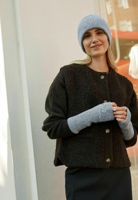 Schwarze, strukturierte Wolljacke mit Knopfschluss, kombiniert mit grauen gerippten Fingerhandschuhen und einer hellblauen Strickmütze.