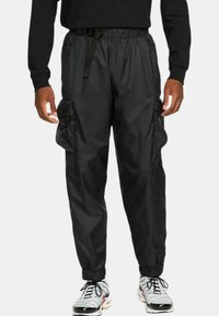 Svarta, lätta cargobyxor i nylon med elastiska muddar och midja. Har två sidofickor och justerbart bälte. Slät textur.