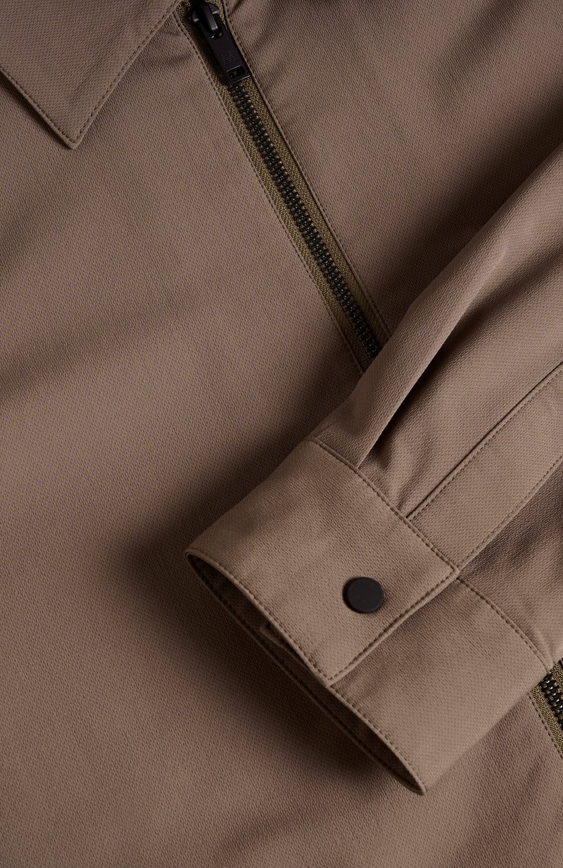 Veste zippée marron avec une finition texturée, dotée d'un col, de détails de manches plissées et d'un accent de bouton noir.