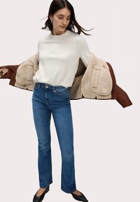 Světlý béžový top s dlouhým rukávem, modré zvonové džíny z denimu a hnědý kabát s beránkovou podšívkou. Outfit doplňují černé baleríny.