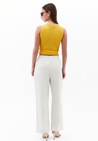 Gul ribbad linne i kombination med lösa krämfärgade byxor. Byxorna har dragsko i midjan och bakfickor, tillsammans med klacksandaler.