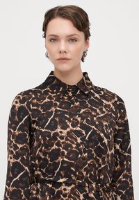 Rochie camasă cu mânecă lungă, cu un model de leopard, având o bază neagră și accente maro și bej, guler și închidere cu butoane.