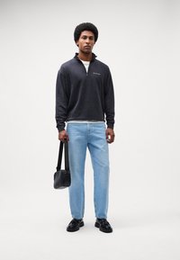 Mørkegrå zip-up sweatshirt, lyseblå jeans, sorte sko og en sort crossbody taske. Glat stof med en afslappet pasform og minimal branding.