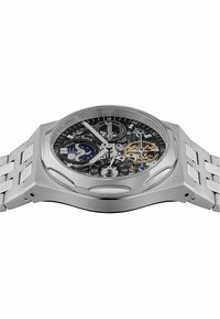 Montre en acier inoxydable argenté avec un cadran squelette rond, mettant en avant des accents noirs, des aiguilles lumineuses, une lunette à motif et un bracelet en maillons métalliques.