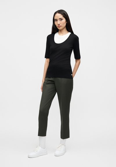 Μαύρο κοντομάνικο τοπ με λαιμόκοψη σε σχήμα στρογγυλού ντεκολτέ, σε συνδυασμό με χακί στενά, καμπυλωτά παντελόνια. Λευκά αθλητικά παπούτσια και λευκές κάλτσες μήκους έως τον αστράγαλο εμφανείς.