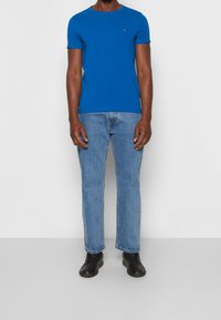 T-shirt en coton bleu avec un col rond, associé à un jean en denim bleu clair et des baskets noires à lacets. Aucune motif ou accent visible.