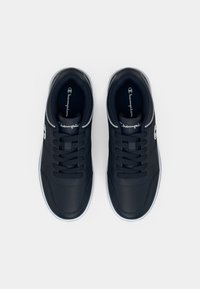 Granatowe tenisówki o gładkiej, fakturowanej powierzchni, białej podeszwie, sznurowanym fasonie oraz srebrnych detalach przy pięcie.