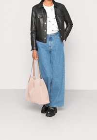Chaqueta de cuero negra sobre una camiseta blanca con un patrón multicolor, jeans de pierna ancha azules y un bolso de ante rosa pálido. Zapatos de plataforma negros.