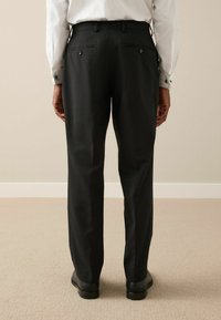 Fekete, egyenes szabású nadrág, két hátulsó zsebével, gombokkal és sima felülettel. Világos színű inggel viselve.