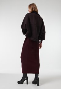 Chaqueta oversized de color marrón oscuro con mangas anchas, combinada con una falda acanalada burdeos. Un par de botas negras de plataforma hasta el tobillo completan el conjunto.
