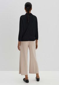 Un haut noir à manches longues avec une coupe décontractée, associé à un pantalon large beige clair et des chaussures noires à enfiler. Texture de tissu lisse.