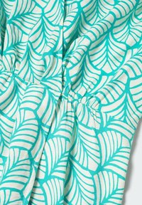 Tissu turquoise avec un motif de feuilles blanches, orné de détails froncés qui rehaussent la texture. Le motif varie avec des lignes courbes et des bords nettes.