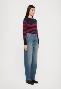 Un maglione a righe blu navy e rosse con maniche lunghe, abbinato a jeans a vita alta di colore blu chiaro con gamba larga, indossato con stivali neri alla caviglia.