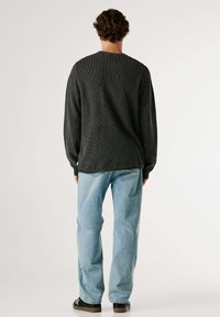 Pull texturé gris foncé à manches longues, associé à un jean bleu clair ample et des chaussures noires. Étiquette visible sur l'ourlet du pull.