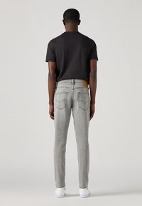 Wąskie jasnoszare dżinsy z brązową skórzaną naszywką na pasku, tylne kieszenie z detalem w postaci przeszycia logo, zestawione z czarnym t-shirtem.