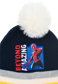 Berretto a maglia blu navy con pompon bianco, dotato di una toppa di Spider-Man e scritta "BEYOND AMAZING" in rosso e bianco. Design con bordo a strisce.
