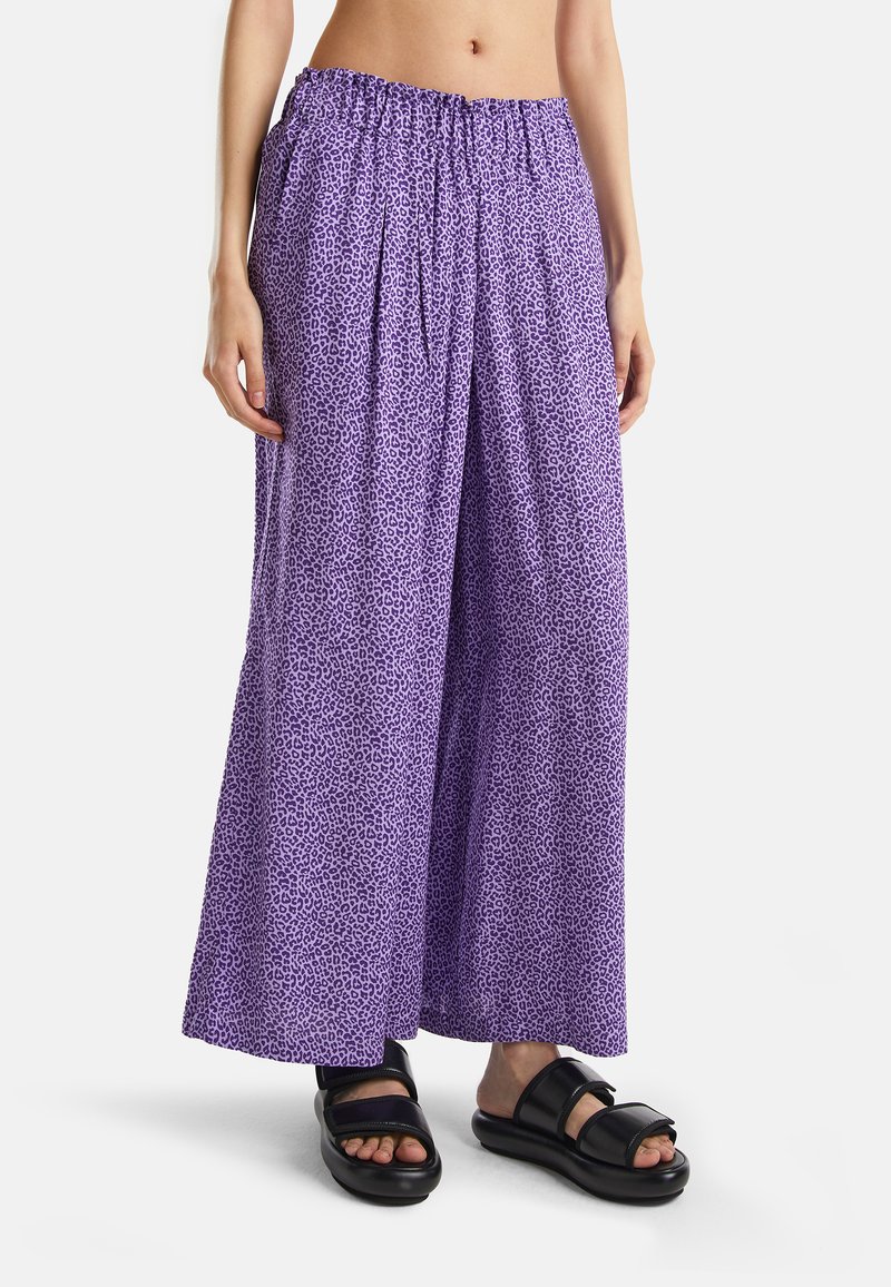 Pantalons larges violets avec un motif léopard, dotés d'une taille élastique. Associés à des sandales noires, présentant une semelle plate.
