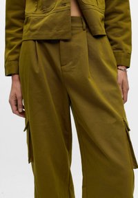 Pantalons cargo verts olive avec une coupe décontractée, présentant des poches latérales, des plis et un tissu texturé. La taille est ajustée avec des passants de ceinture.