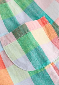 Gros plan d'une poche cousue sur un tissu à carreaux pastel multicolore avec des carrés verts, roses, orange et jaunes.