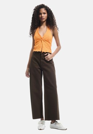Top arancione con collarino, dalla finitura testurizzata e con dettaglio annodato sul davanti, abbinato a pantaloni a gamba larga marroni scuri e sneakers bianche.
