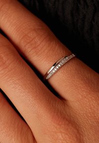 Silver ring with a smooth, polished band and a row of small, clear gemstones along one side. Set against a hand skin tone.