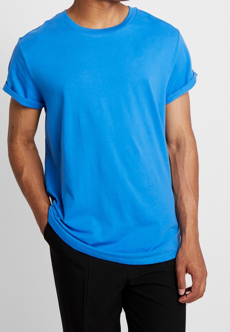 Blå crew-neck t-shirt i mjuk bomull, med rullade ärmar och avslappnad passform. Slät textur, inga synliga mönster eller designer.